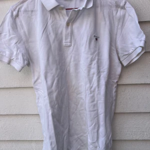 Vit kortärmad pikétröja från Gant - Säljer en klassisk vit pikétröja från Gant. Den har korta ärmar och en liten broderad logga på bröstet. Perfekt för en stilren och avslappnad look. Tröjan är i bomull och passar bra till både vardag och fest. Aldrig använd 