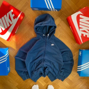 Blå hoodie från Nike - Säljer en snygg och bekväm blå hoodie från Nike. Den har en dragkedja framtill och en huva med snören. Perfekt för streetstyle och casual stil. Hoodien är i storlek L och är i perfekt skick🤩
