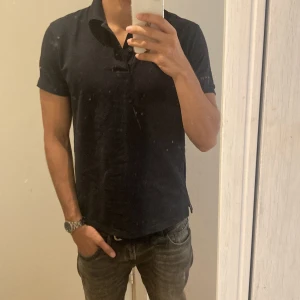 Svart pikétröja från Uniqlo - Säljer en stilren mörkblå pikétröja från Uniqlo i storlek S. Tröjan är kortärmad och har en klassisk krage med knappar. Perfekt för både vardag och lite mer uppklädda tillfällen. Skön och enkel att matcha med det mesta! Nyskick och passar mig som är 180