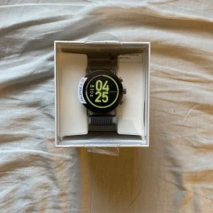 Svart smartklocka från Skagen - Säljer en snygg och modern svart smartklocka från Skagen. Klockan har en rund urtavla med digital display och ett stilrent armband i svart mesh. Perfekt för både vardag och fest! Klockan kommer med originalförpackning och laddare. Använd en gång