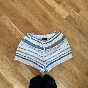 Randiga shorts från Polo Ralph Lauren - Säljer ett par snygga och bekväma shorts från Polo Ralph Lauren. De är vit- och blårandiga med en elastisk midja och snörning för perfekt passform. Perfekta för en avslappnad sommardag!