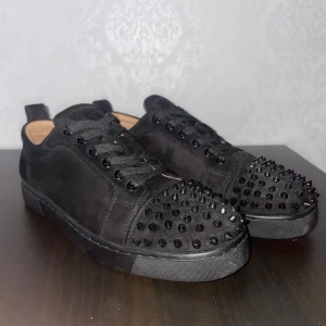 Louboutin Skor  - Snygga svarta sneakers från Christian Louboutin med nitar på tåpartiet. Skorna har en klassisk röd sula och är tillverkade i mocka. Perfekta för att ge din outfit en edgy touch. Storlek 41 men passar 42 också , lite använda men på ett bra sätt , de är i bra skick och ett bra fynd. Skriv för mer info! 