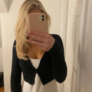 Svart kofta - Säljer en stilren svart kofta med knappar framtill. Perfekt för lager-på-lager och passar till många olika outfits. Koftan har långa ärmar och är kort.