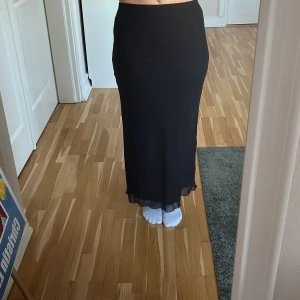 Svart långkjol  - Elegant svart långkjol från Shein i ett mjukt och flödande material. Den är i storlek M och har en lätt transparent nederdel för en extra touch. 