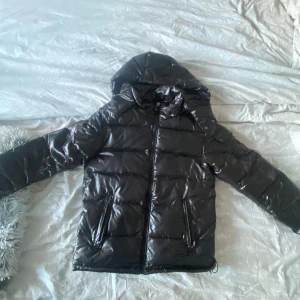 Svart pufferjacka med huva - Snygg svart pufferjacka med glansig yta, det finns en ficka på ena ermen. Aldrig använd!! 💕