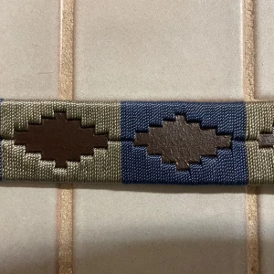 Mönstrat bälte med guldfärgat spänne - Snyggt  brunt bälte med ett mönster i beige och blått. Bältet har ett guldfärgat spänne och är tillverkat i skinn. Perfekt för att ge en stilfull touch till din outfit.