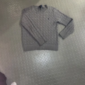 Grå stickad tröja från Polo Ralph Lauren - Snygg grå stickad tröja från Polo Ralph Lauren med kabelstickat mönster. Tröjan har långa ärmar och en rund halsringning, perfekt för kyligare dagar. passar dig som är ca 175-185 . Om priset inte passar är det bara att skriva. MVH 