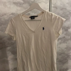 Vit t-shirt från Ralph Lauren  - Säljer en vit t-shirt från Ralph Lauren  i 100% bomull. T-shirten har en v-ringad design och en blå loga på bröstet. 