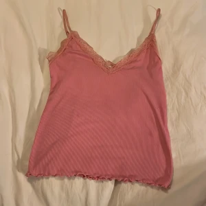 Rosa ribbad linnetopp med spetsdetaljer - Söt rosa ribbad linnetopp med smala axelband och spetsdetaljer vid halsringningen. Perfekt för varma sommardagar eller som ett lager under en kofta.