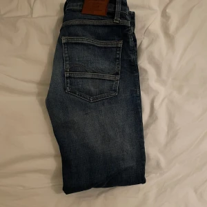 Jack and Jones jeans - Säljer ett par blå jeans med coola slitningar på framsidan. De har en klassisk femficksdesign och en bekväm passform. Perfekta för en avslappnad stil. W30 L32