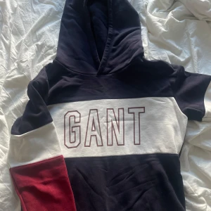 Flerfärgad hoodie från GANT - Snygg hoodie från GANT i marinblått, vitt och rött. Den har en stor logga på bröstet och en bekväm huva. Perfekt för en avslappnad stil. Nyskick endast använd ca 3 gånger. 