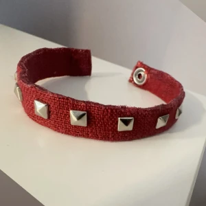 Rött armband med nitar - Snyggt rött armband med silverfärgade nitar. Perfekt för att ge en edgy touch till din outfit. Armbandet har en praktisk tryckknapp för enkel på- och avtagning. 17cm