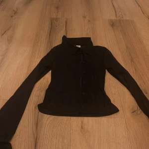 Svart långärmad tröja från H&M Divided - Säljer en svart långärmad tröja från H&M Divided i storlek XXS. Tröjan har knappar framtill och en klassisk krage, perfekt för en stilren look.