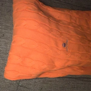 Orange stickad tröja från Gant - Säljer en snygg orange stickad tröja från Gant med kabelstickat mönster. Tröjan har långa ärmar och en rund halsringning. Perfekt för att hålla sig varm och stilren under kyligare dagar. 