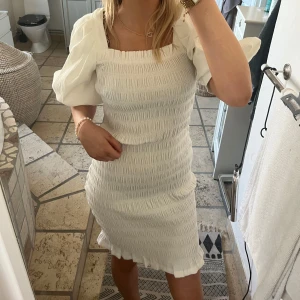 Vit klänning från A View - Säljer en stilren vit klänning från A View med puffiga kortärmar och en smickrande tight passform. Klänningen har en texturerad yta som ger en unik look. Perfekt för sommarens alla tillfällen! Helt ny!! nypris 900kr!! perfekt till studenten!!🩷