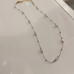 Halsband med pärlor och gulddetaljer - Elegant halsband  med vita pärlor och små gulddetaljer. Perfekt för att ge en touch av lyx till din outfit. Kedjan är tunn och smidig, vilket gör den bekväm att bära hela dagen.