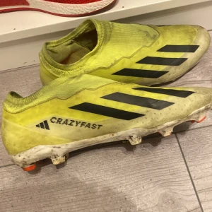 Crazyfast fotbollsskor från Adidas - Säljer ett par gula Adidas fotbollsskor med svarta detaljer och texten 'Crazyfast'. Skorna har en strömlinjeformad design utan snörning och är perfekta för snabba rörelser på planen.