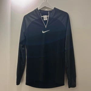 Svart långärmad tröja från Nike - Säljer en svart långärmad tröja från Nike med Dri-FIT-teknologi. Tröjan har en halv dragkedja framtill och det ikoniska Nike-logotypen på bröstet. Perfekt för träning och sportiga aktiviteter.