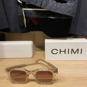 Transparenta solglasögon från Chimi - Snygga transparenta solglasögon från Chimi med fyrkantig form och bruna tonade linser. Perfekta för en stilren look. Kommer med ett vitt fodral för säker förvaring.