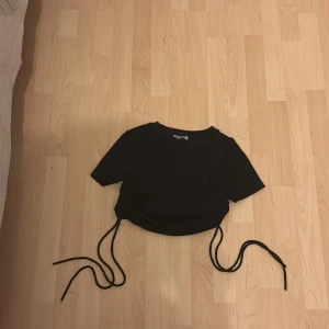 Svart kortärmad topp med knytband - Snygg svart topp med korta ärmar och knytband i sidorna för en justerbar passform. Perfekt för en trendig look.
