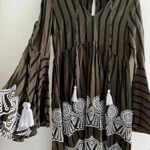 Grön klänning med broderi - Bohemisk klänning med fina broderidetaljer och tofsar. Utsvängda armar. Knappt använd. Djur- och rökfritt hem.