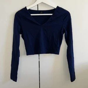 Mörkblå croppad topp - Snygg mörkblå croppad topp med v-ringning och långa ärmar. Perfekt för en stilren look. Strl S, men är mer som en XS. Aldrig använd, i nyskick. Tryck gärna på ”köp nu”.