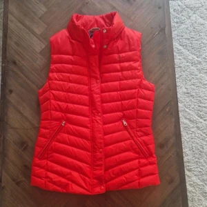 Röd dunväst från GANT - Snygg röd dunväst från GANT med dragkedja och knappar. Perfekt för kyliga dagar med sin quiltade design och praktiska fickor.