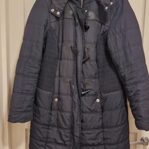 Svart kappa från Bodyflirt - Snygg svart kappa från Bodyflirt med knappar och dekorativa snördetaljer. Jackan har långa ärmar och en quiltad design som ger extra värme. Perfekt för kyliga dagar.