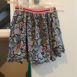 Färgglad kortkjol med hjärtmönster - Säljer en färgglad kortkjol med ett lekfullt hjärtmönster i rosa, blått och gult. Kjolen har en elastisk midja med rosa och svarta ränder. Perfekt för en poppig och rolig stil! Den ser väldigt skrynklig och missfärgad ut men den är inte det jag lovar. Väldigt fin kjol. Kan diskutera pris, du står för frakten❣️