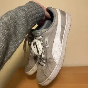 Säljer ett par stilrena grå sneakers från Puma med vit sula och klassisk logga på sidan. Skorna har snörning och är perfekta för en avslappnad stil. De är bekväma och passar till många olika outfits.