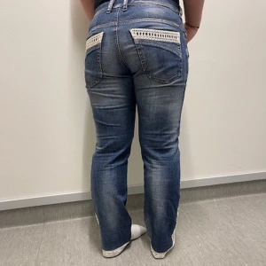 Blå jeans med spetsdetaljer - Snygga blå jeans med spetsdetaljer på bakfickorna och längs sidorna. De har en klassisk femficksdesign och en bekväm passform. Perfekta för en avslappnad stil. Märke diesel, köpta secondhabd omsydda av mined uf.