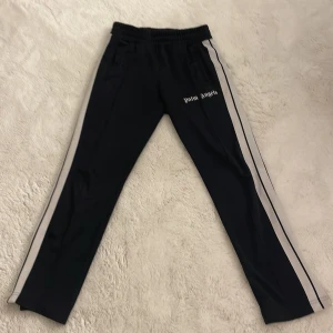 Svarta träningsbyxor från Palm Angels - Snygga svarta träningsbyxor från Palm Angels med vita sidoremsor. Märkeslogga på benet ger en extra touch. Självklart äkta. Pris kan diskuteras vid snabb affär