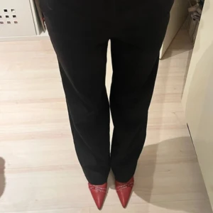 Svarta kostymbyxor - Snygga svarta kostymbyxor med en klassisk straight passform. Perfekta för en stilren look. Byxorna är midwaist och är tillverkade i ett elegant material som ger en sofistikerad känsla.