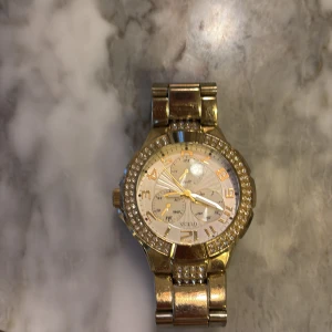 Guldfärgad klocka från Skmei - Snygg guldfärgad klocka från Skmei med glittrande detaljer runt urtavlan. Klockan har en metallarmband och tydliga siffror på urtavlan. Perfekt för att lägga till lite bling till din stil.