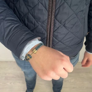 Grönt armband med ankardetalj - Snyggt grönt armband med en unik ankardetalj i metall. Armbandet har en stilren design med dubbla band och små metallringar som ger en marin känsla. Perfekt accessoar för en avslappnad stil. 