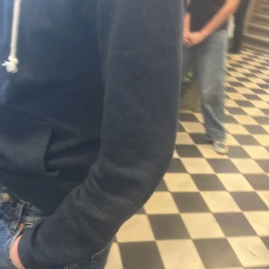 Mörkblå hoodie med snören - Säljer en mörkblå hoodie med snören i huvan. Perfekt för en avslappnad stil. Den har en klassisk passform och en stor ficka framtill.