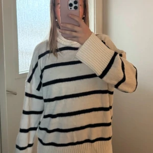 Randig stickad polotröja - Säljer en mysig stickad polotröja i vitt med svarta ränder. Tröjan har långa ärmar och en bekväm polokrage. Perfekt för kyliga dagar!              Nopprig men annars fin, inte värdens bästa kvalitet på tröjan därav att stickningen ser lite tun och genomskinlig ut🤍   Jag har varit mycket nöjd med den!  Finns en matchande kjol!!