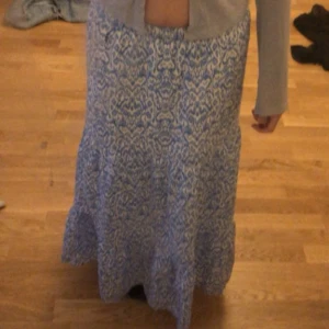 Blåvit långkjol med mönster - Säljer en vacker blåvit långkjol med ett unikt mönster. Kjolen har en bekväm passform och är perfekt för både vardag och speciella tillfällen. Den är tillverkad i ett lätt och luftigt material som ger en skön känsla.