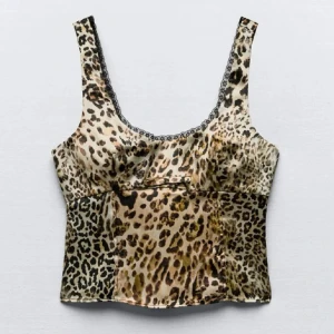 Leopardmönstrad korsettopp med spetsdetaljer - Trendig leopardmönstrad korsettopp med spetsdetaljer längs halsringningen. Toppen har breda axelband och en figurnära passform, perfekt för en djärv look. 