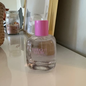 Twilight Mauve parfym - Säljer en elegant parfymflaska från Twilight Mauve. Flaskan är genomskinlig med en ljusrosa kork och text. Perfekt för den som älskar en subtil och fräsch doft. Flaskan har en stilren och modern design som passar fint på sminkbordet.
