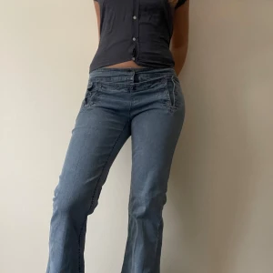 Blå jeans med knappar - Snygga blå jeans med unika knapplösningar och låg midja. Byxorna har en bootcut-modell! En knapp saknas där fram! Midjemått: 38 rakt över innebenslängd 79 cm