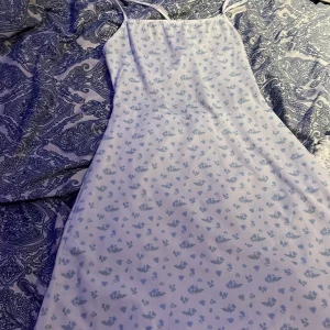 Vit blommig klänning från Only - Söt vit klänning med blå blommor från Only. Den har smala axelband och en öppen rygg med knytband. Perfekt för varma sommardagar. Bara testad