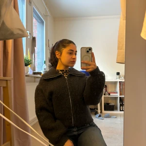 Mörkgrå stickad jacka med dragkedja - Säljer en mysig mörkgrå stickad jacka med dragkedja framtill. Jackan har en hög krage och långa ärmar, perfekt för kyligare dagar. Den har en normal passform och är både stilren och bekväm.