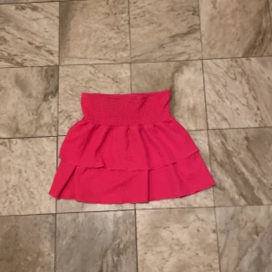 Rosa kjol från Gina Tricot - Säljer en söt rosa kjol från Gina Tricot med volangdetaljer. Kjolen har en elastisk midja för bekväm passform och är perfekt för sommarens varma dagar.