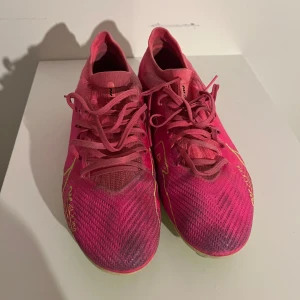 Rosa Nike fotbollsskor - Skorna har en syntetisk ovandel och en limegrön sula med dobbar för bra grepp på planen. Perfekta för fotbollsspelare som vill sticka ut på planen. Lite smutsiga pga konstgräs. Ta bara en borste och borsta lite så går de säkert bort!