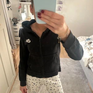 Svart hoodie från Nike - Säljer en svart hoodie från Nike med dragkedja och huva. Perfekt för en avslappnad stil. Den har en vit Nike-logga på bröstet och långa ärmar.