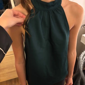 Mörkgrön halterneck top - Snygg mörkgrön ärmlös topp med hög hals och öppen rygg. Perfekt för en kväll ute eller en speciell tillställning. Toppen har en elegant och modern design som framhäver axlarna. Tyvärr lite stor på mig. Strl s men passar nog även m💕
