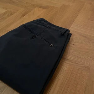 Dondup Chinos – Made in Italy - Material: 100% bomull – högkvalitativ och hållbar	Storlek: 33 – modern och stilren passform Skick: Väldigt fint skick, knappt använda	    Design: Klassisk italiensk elegans Extra: Originalknapp medföljer som reserv  Beskrivning: Snygga och exklusiva chinos från Dondup, tillverkade i Italien. Byxorna kombinerar hög komfort med en tidlös design som passar både vardag och fest. Materialet är mjukt men slitstarkt och ger en perfekt balans mellan stil och funktion.  