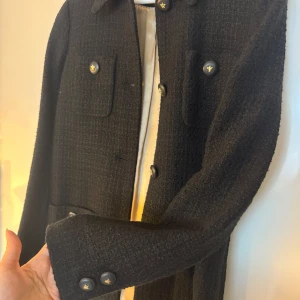 Svart kappa med knappar från Morris - Elegant svart kappa från Morris, med knappar och två bröstfickor. Kappan har en klassisk krage och är perfekt för kyligare dagar. Den har en stilren design som passar till många olika tillfällen.