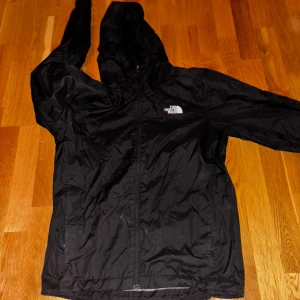Svart vindjacka från The North Face - Säljer en svart vindjacka från The North Face med huva och dragkedja. Jackan har en meshfoder på insidan för extra komfort och ventilation. Perfekt för blåsiga dagar och utomhusaktiviteter. Ser ut som att det är fläckar fram på första bilden men det är blixten som gjort att det blivit så. Skick 9.5/10 Size S men sitter ganska stort så mellan S och M typ